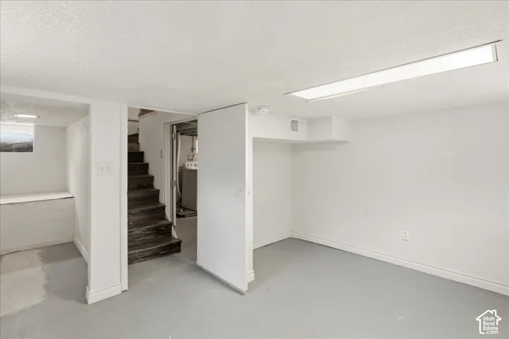 Finished basement area featuring a utility closet, painted concrete flooring, and an exposed wood staircase