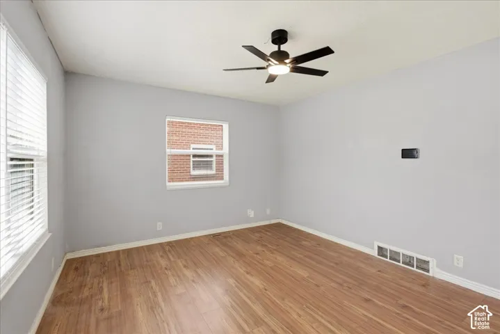 Spacious room featuring wood-finish flooring, light gray wall paint, and a modern ceiling fan with integrated lighting