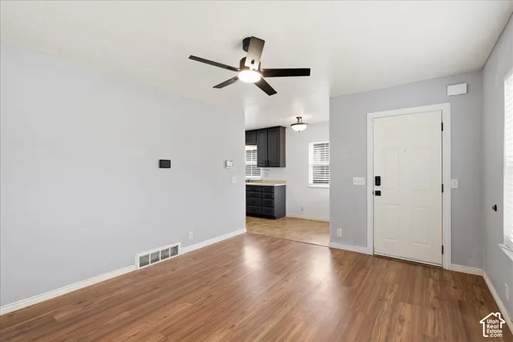 Expansive living area featuring wood-finish flooring, a contemporary ceiling fan with lighting, and a white paneled entry door