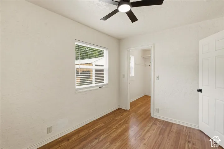 Interior room featuring wood-finish flooring, a window with horizontal blinds, and a ceiling fan