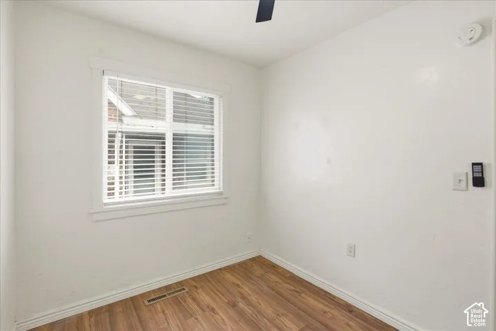 Room featuring wood-finish flooring, white walls, and a window with blinds