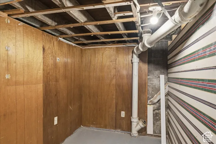 Basement area with wood paneling, exposed ceiling joists, and concrete flooring