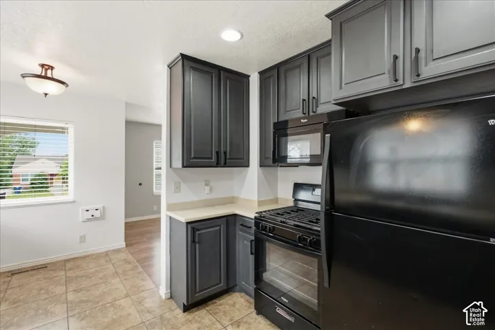 Kitchen featuring dark gray cabinetry with black hardware, light-toned countertops, a black gas range, and a black microwave