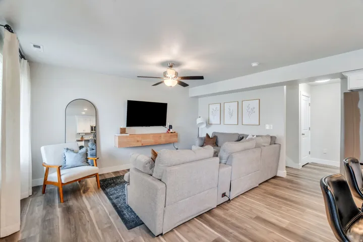 Spacious living area featuring light wood-finish flooring, a contemporary ceiling fan with integrated lighting, and neutral wall tones