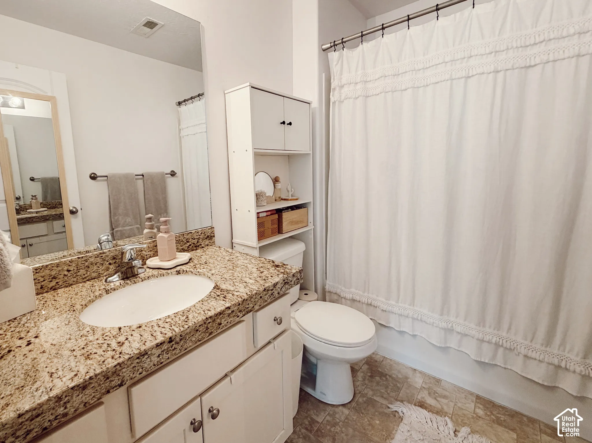 Bathroom featuring a vanity with a granite-look countertop and an integrated sink, white cabinetry with silver-tone pulls, a built-in wall cabinet with open shelving, and a shower-over-tub combination