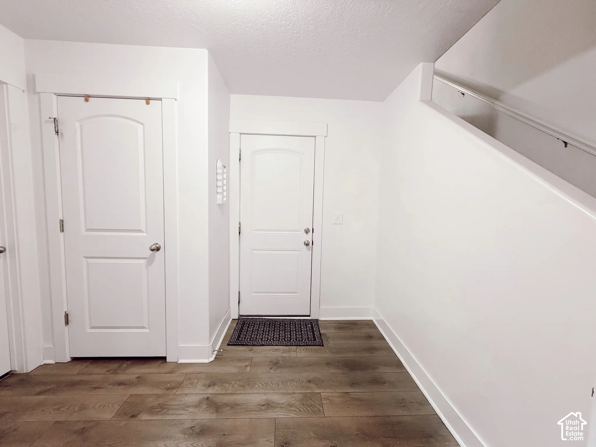 Wood-finish flooring, white walls, white doors with paneling, and a staircase with a white handrail