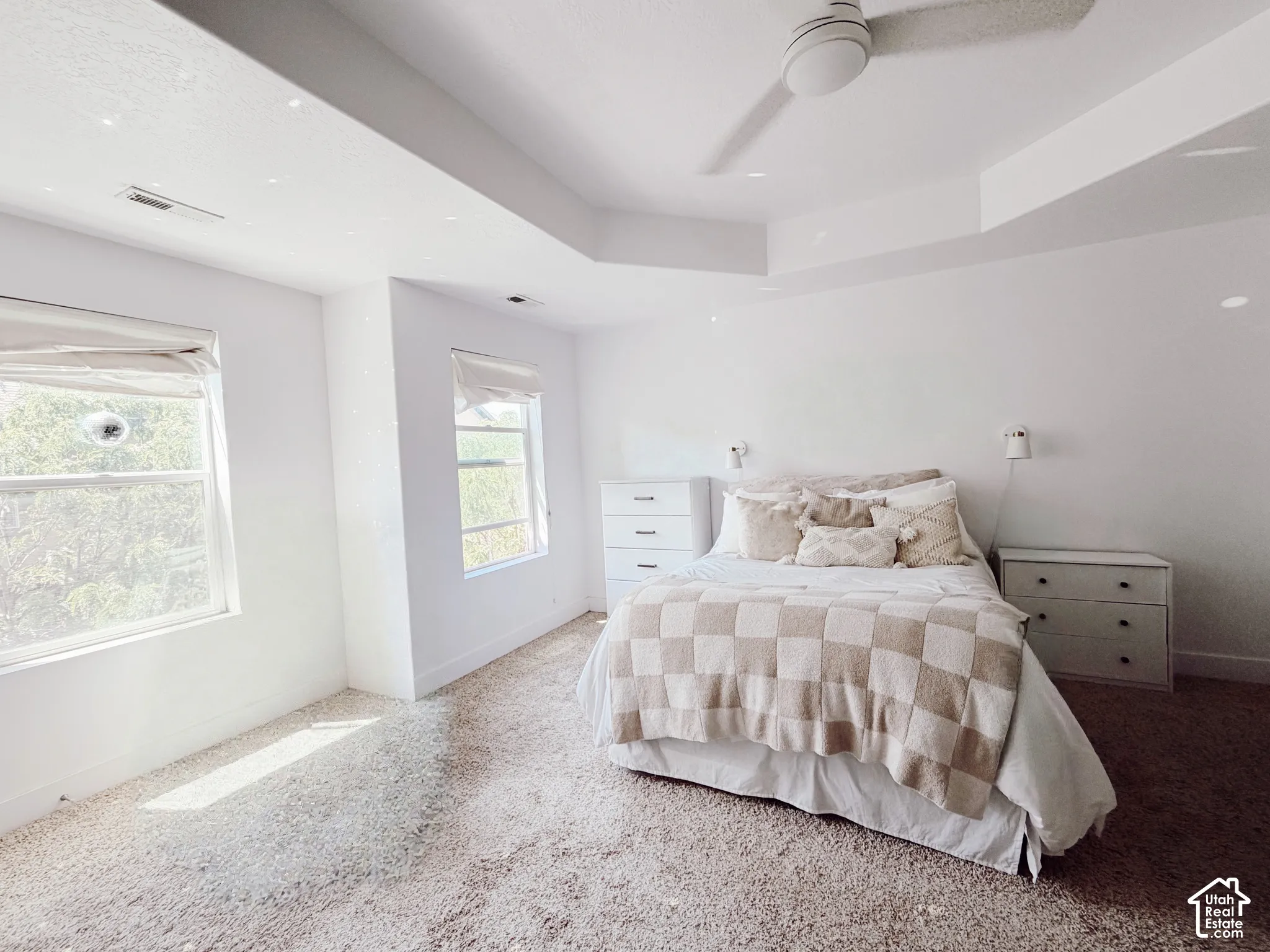 Recessed lighting, ceiling fan, and tray ceiling in a carpeted room with multiple windows