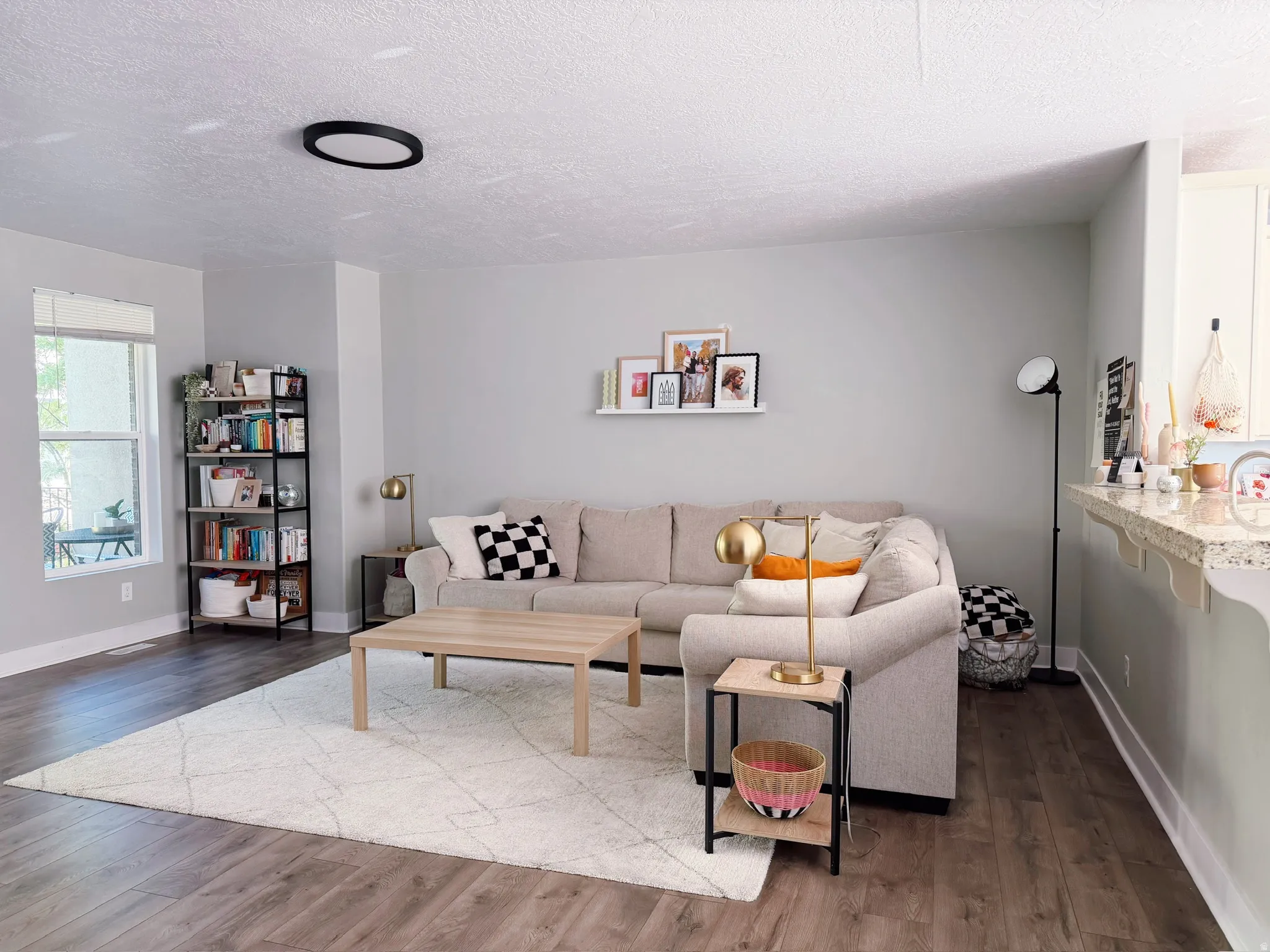Open-concept living area featuring wood-finish flooring, a large window, a ceiling-mounted light fixture, and light-toned walls