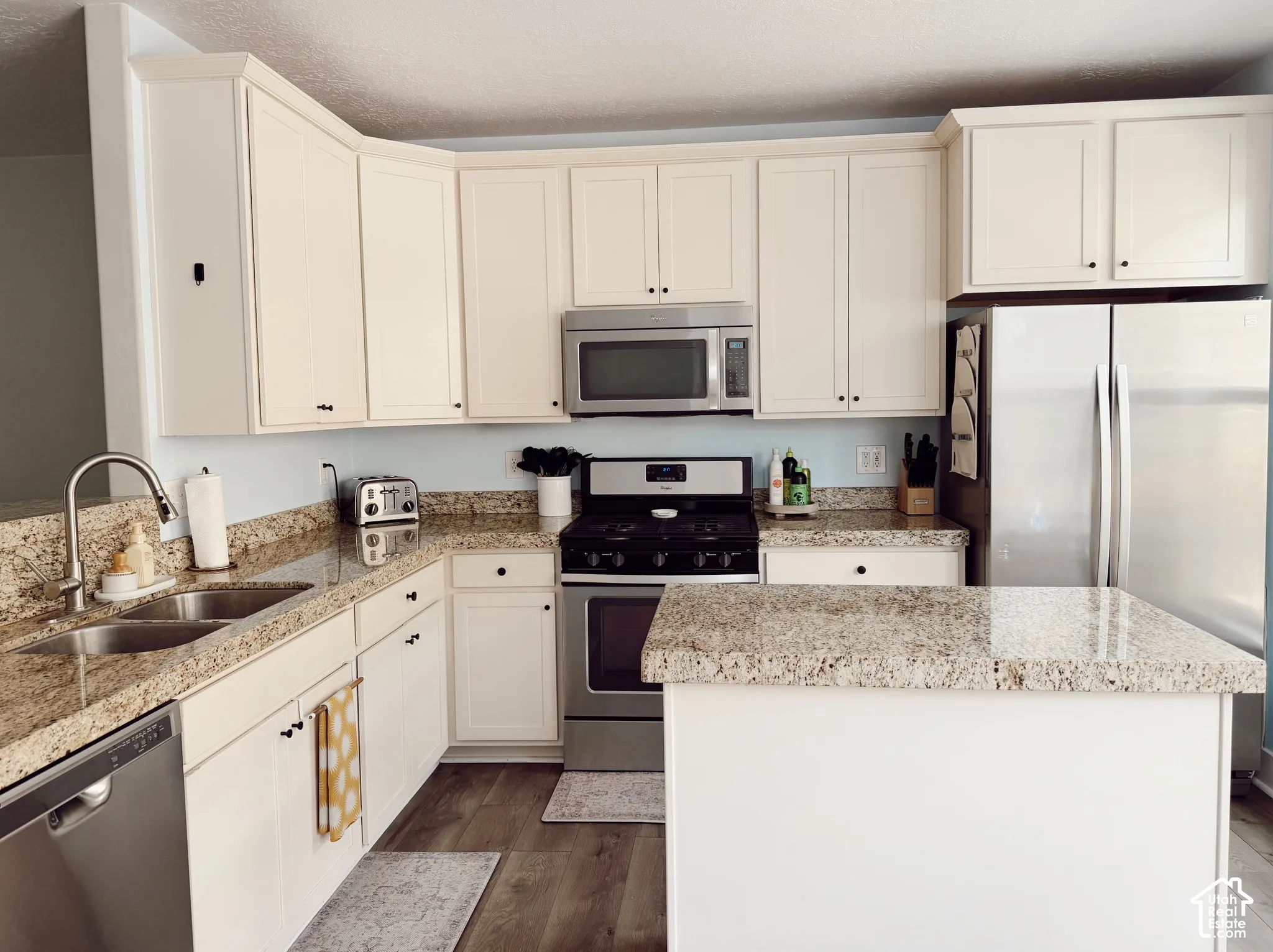 Kitchen featuring cream cabinetry, granite countertops, stainless steel appliances, a double basin sink, and wood-finish flooring
