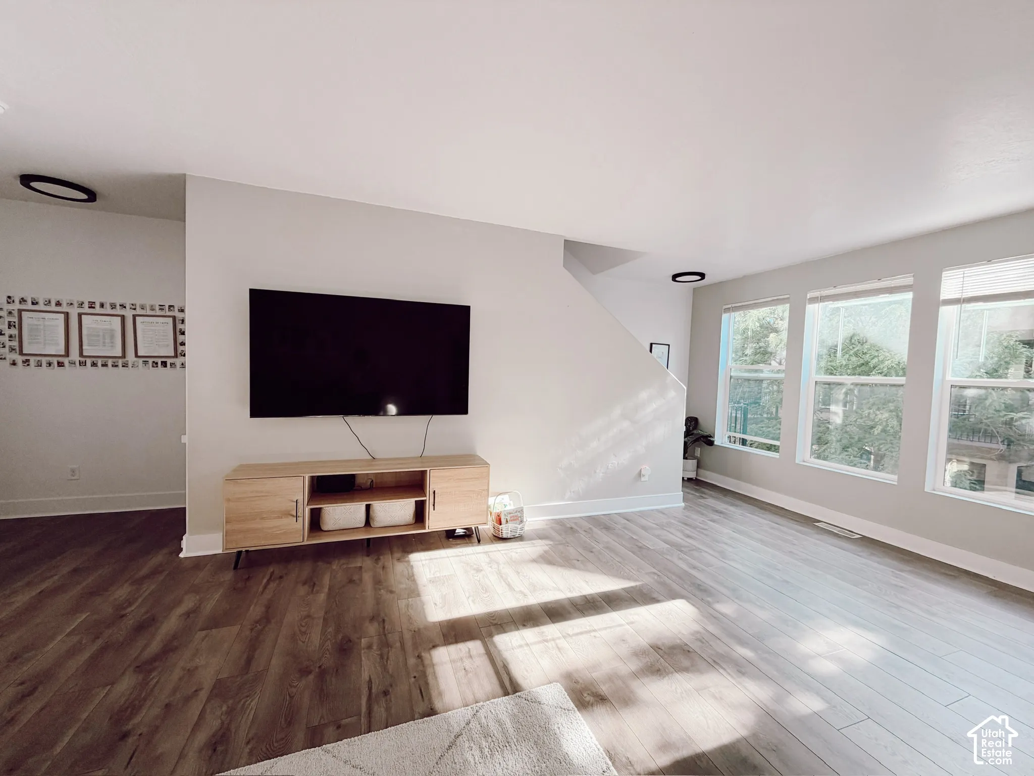 Spacious living area featuring wood-finish flooring, ample natural light from multiple windows, and a neutral color palette