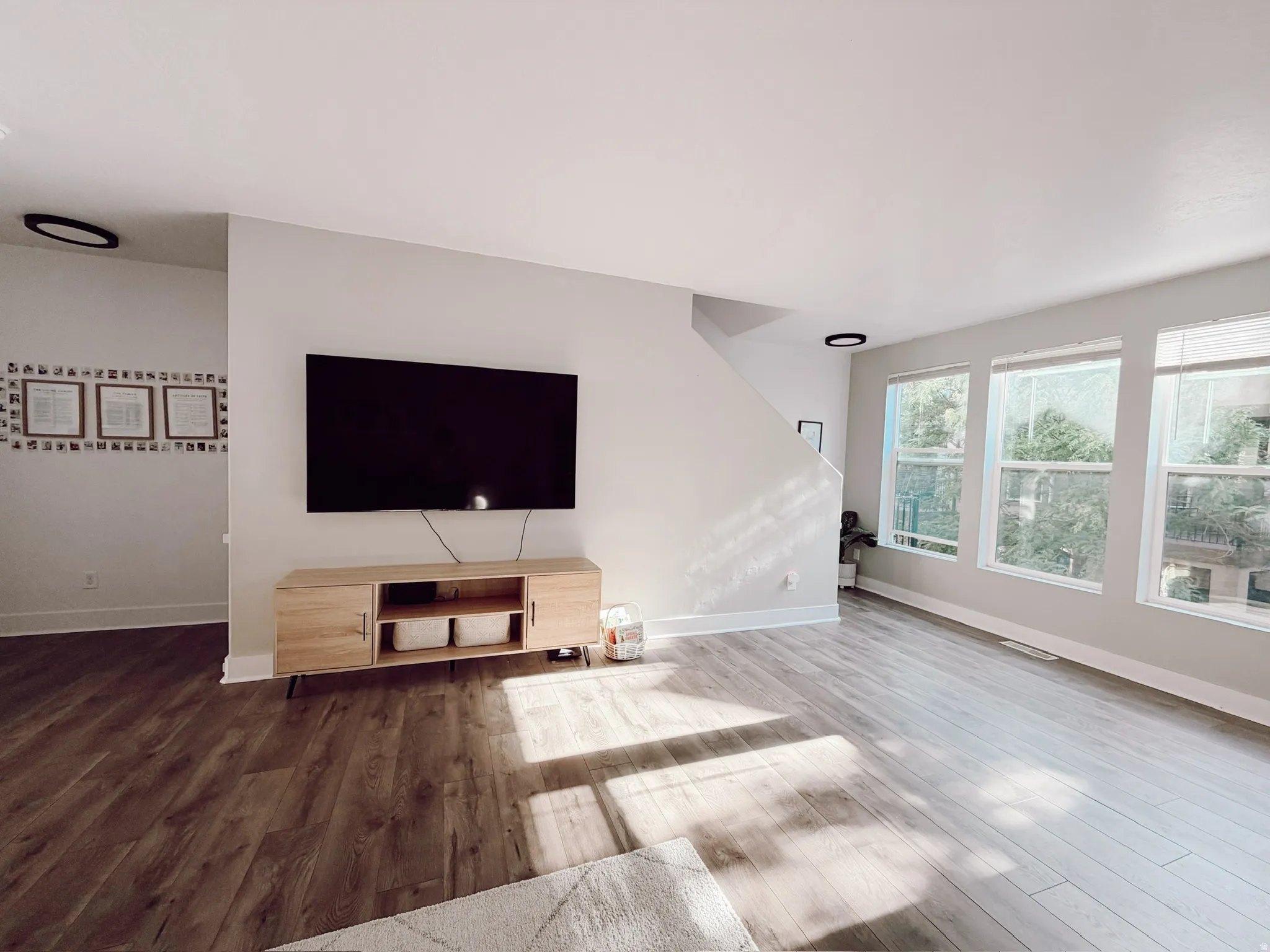 Spacious living area featuring wood-finish flooring, ample natural light from multiple windows, and a neutral color palette