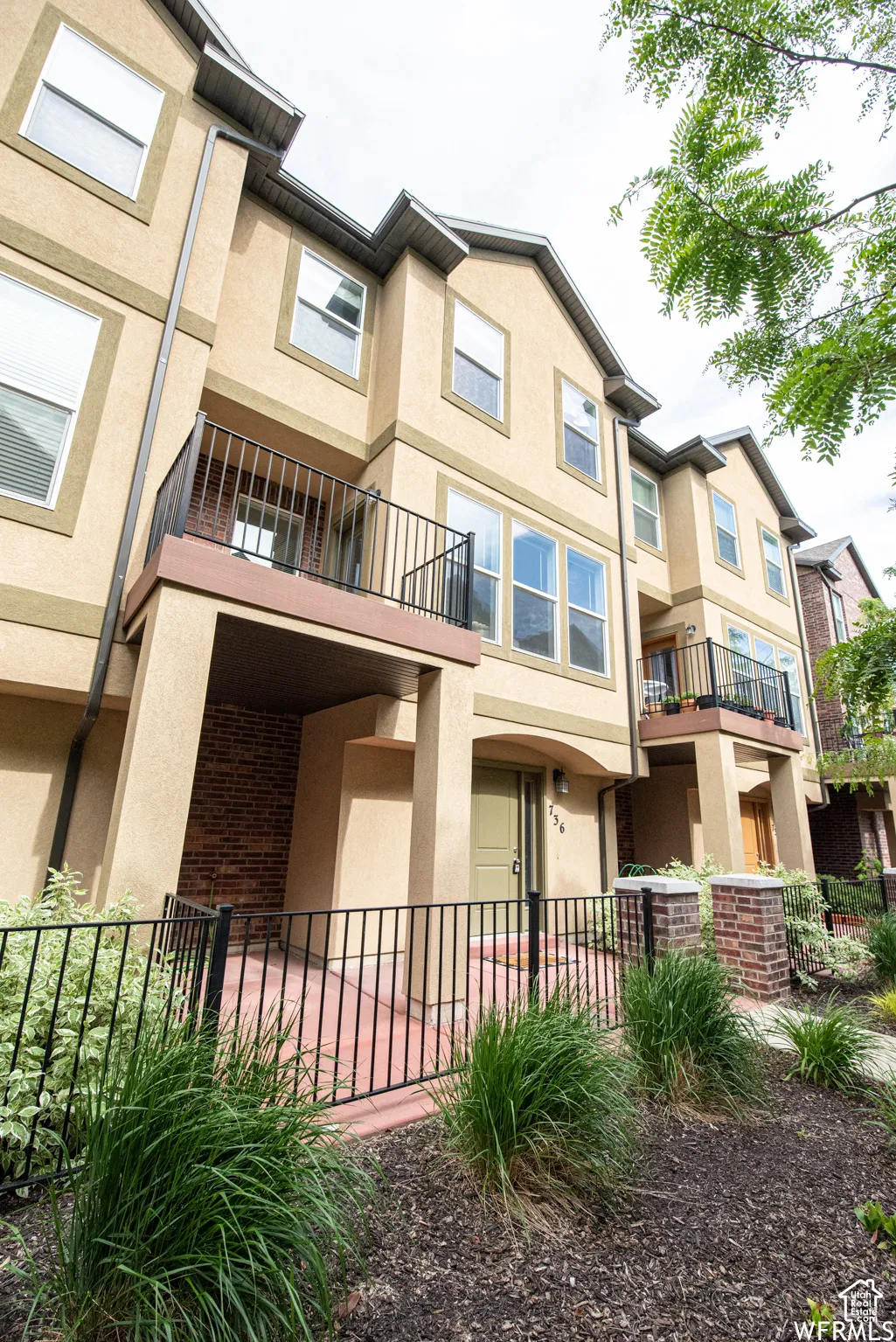 Multi-level townhouse exterior featuring stucco siding, multiple windows, and a private balcony with black railings