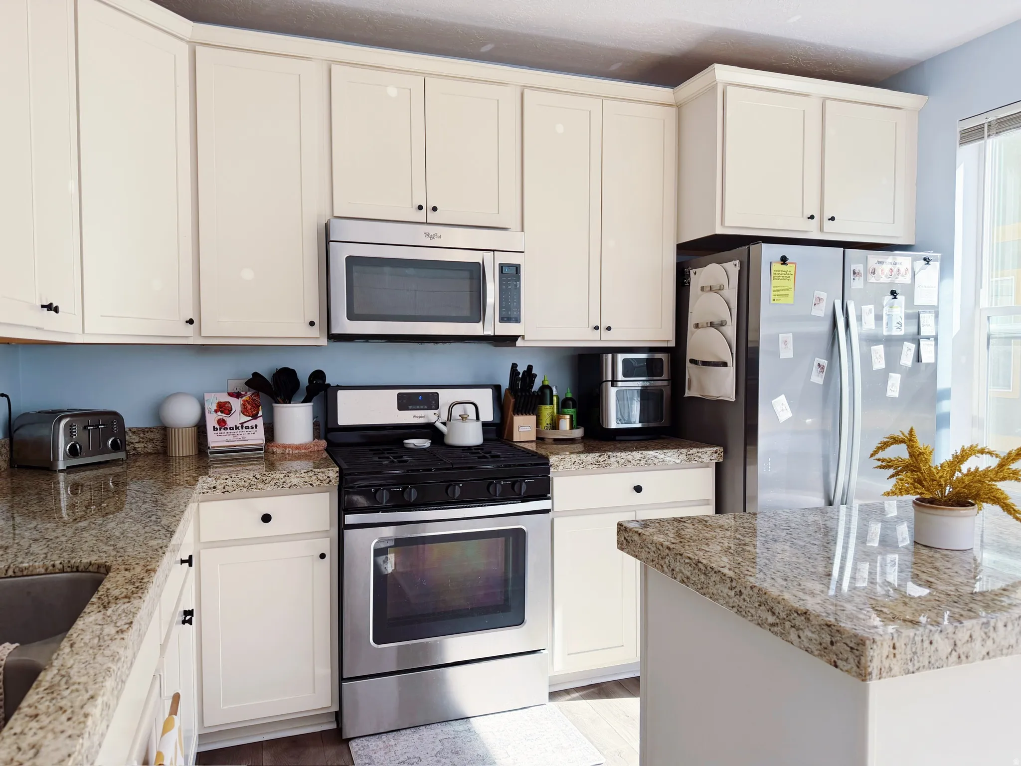 Kitchen featuring cream-colored cabinetry with dark hardware, granite countertops, a stainless steel gas range, and a stainless steel over-the-range microwave