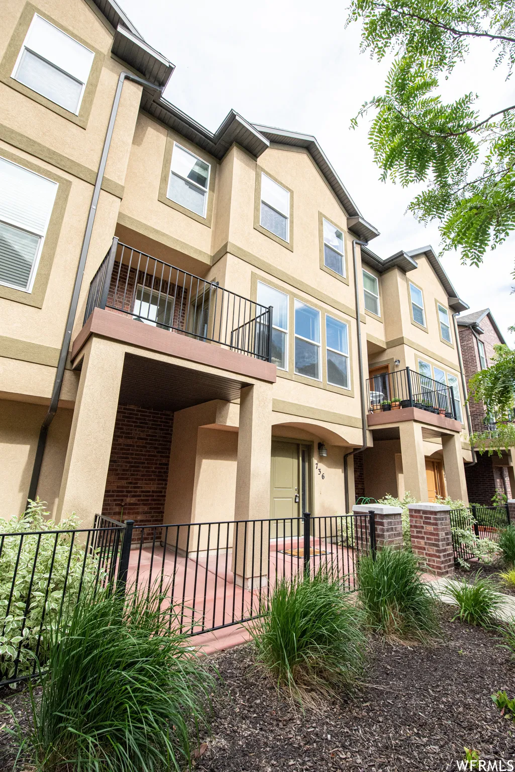 Multi-level townhouse exterior featuring stucco siding, multiple windows, and a private balcony with black railings
