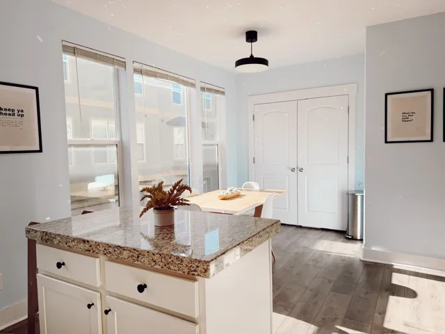 Kitchen island with a granite countertop, white cabinetry with black hardware, and wood-finish flooring