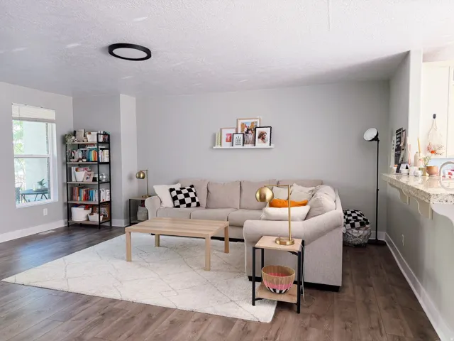 Open-concept living area featuring wood-finish flooring, a large window, a ceiling-mounted light fixture, and light-toned walls