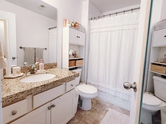Master bathroom featuring a granite-look countertop, undermount sink, white cabinetry with silver hardware, an integrated shower/tub combination, and a white over-toilet storage unit