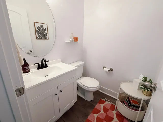 Half bath and white vanity with integrated sink, black faucet, and wood-finish flooring