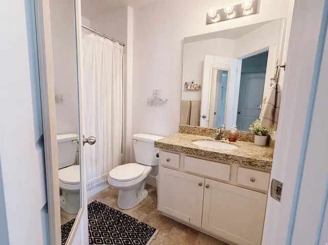 Main bathroom featuring a light-toned vanity with a granite-style countertop, an undermount sink, and a chrome faucet