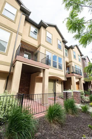 Multi-level townhouse exterior featuring stucco siding, multiple windows, and a private balcony with black railings