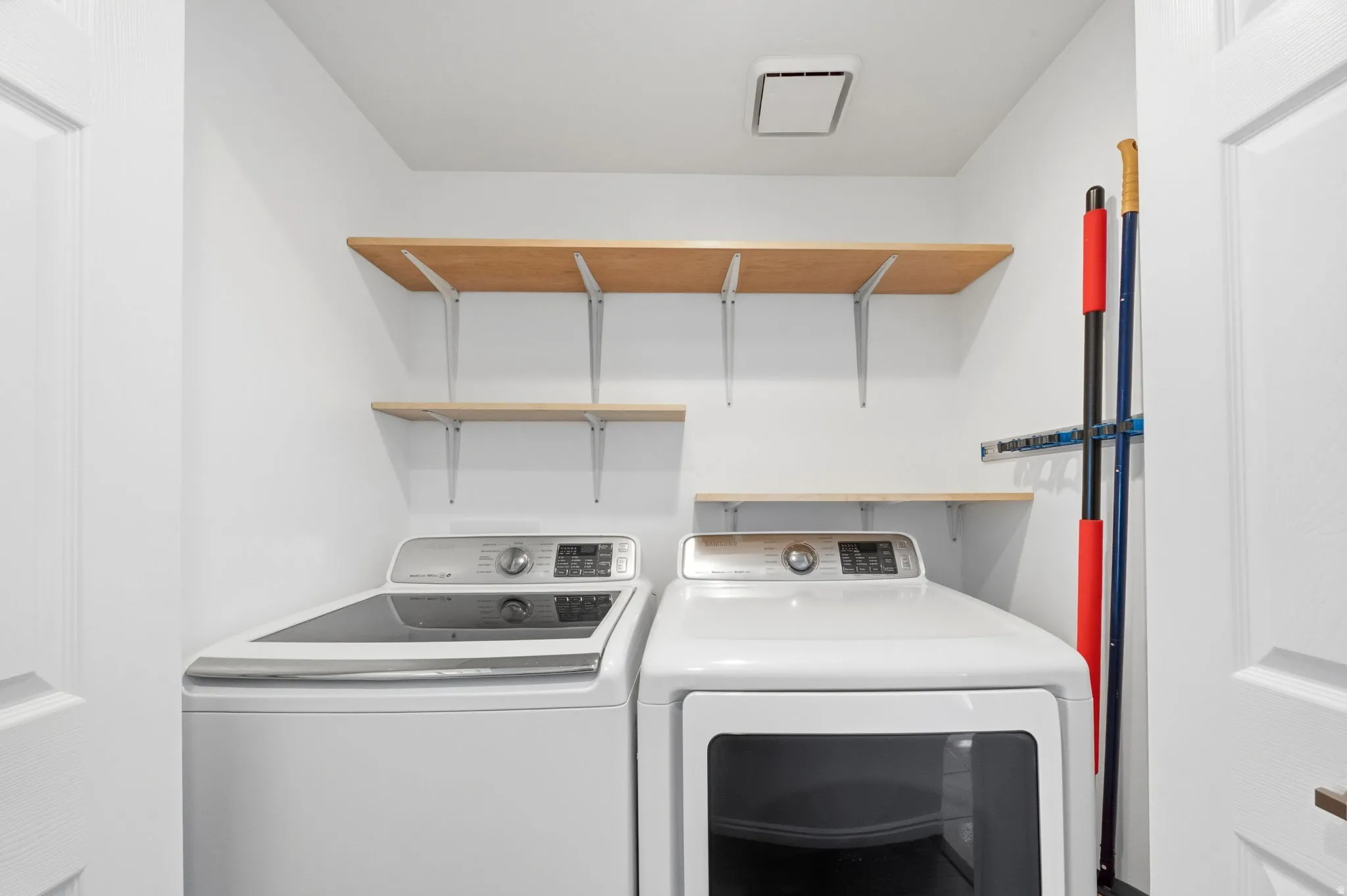 Dedicated laundry space featuring white walls, two appliances, and light wood-finish shelving