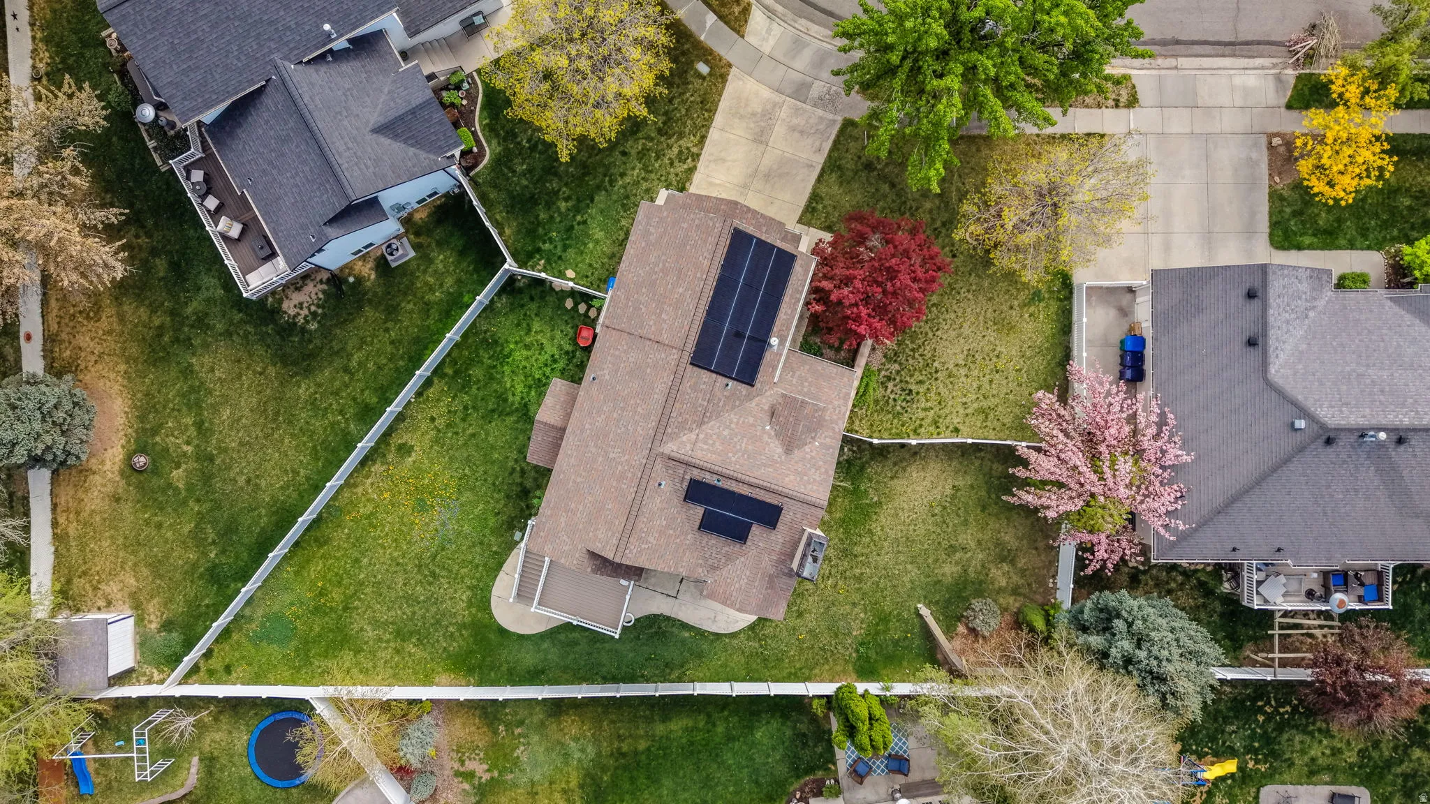 Aerial perspective showcasing a property with a brown shingle roof, integrated solar panels, and a concrete driveway