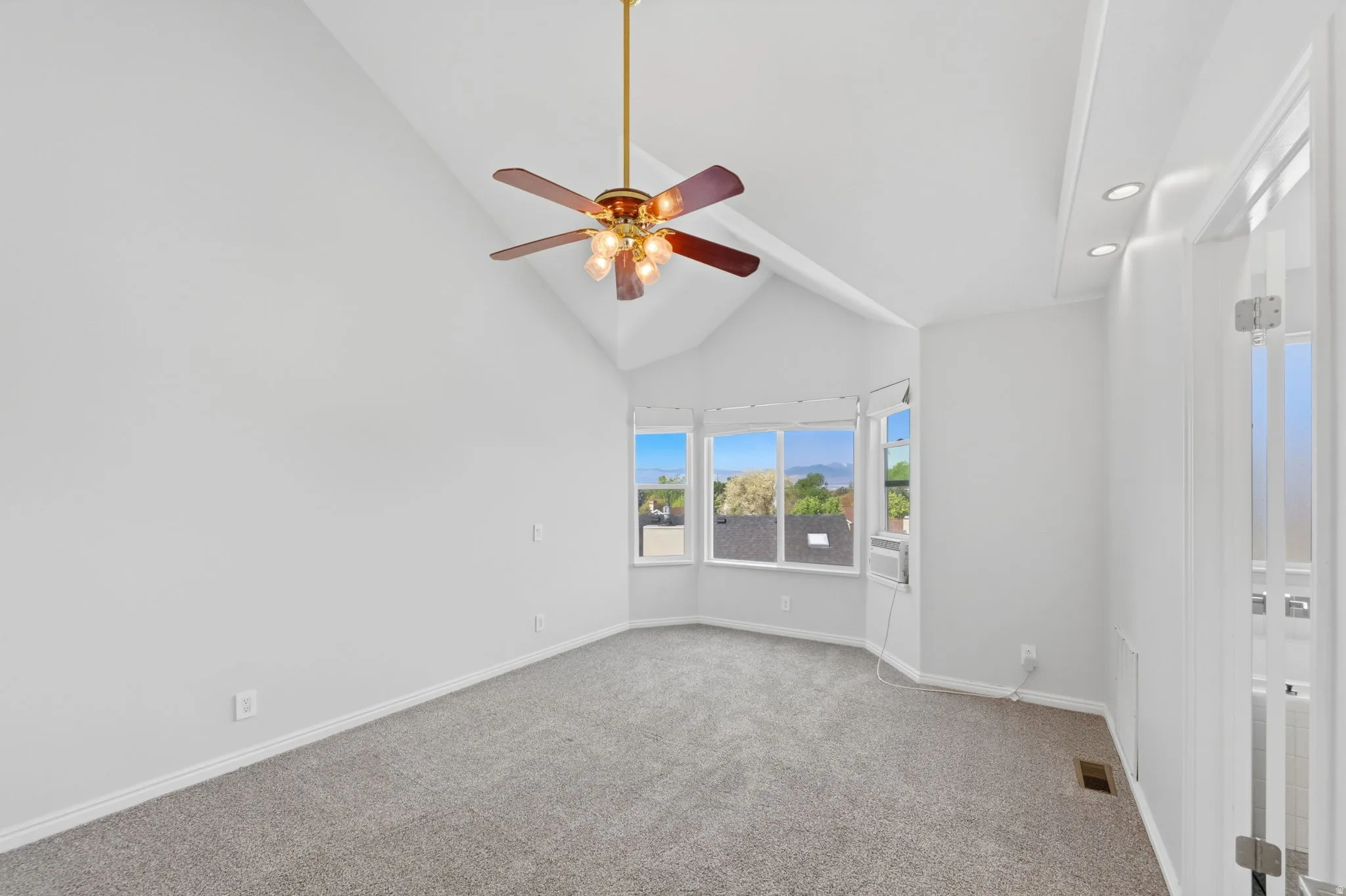 Vaulted ceiling room featuring a bay window, ceiling fan with light fixture, gray carpet, and white trim