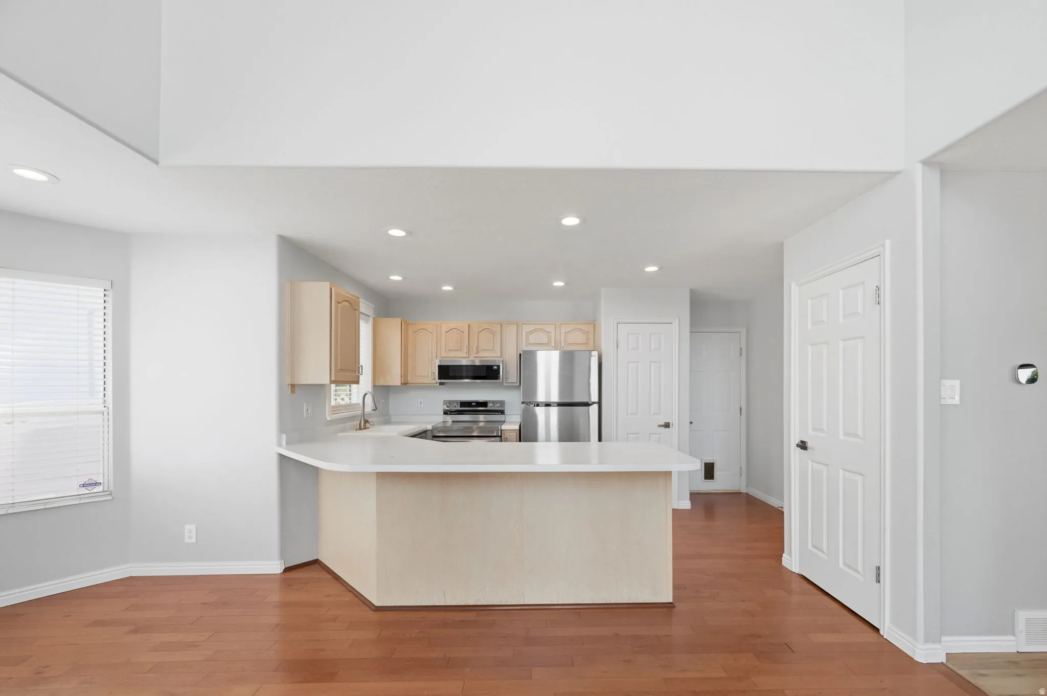 Open-concept kitchen featuring light wood cabinetry, stainless steel appliances, a white countertop, and recessed lighting