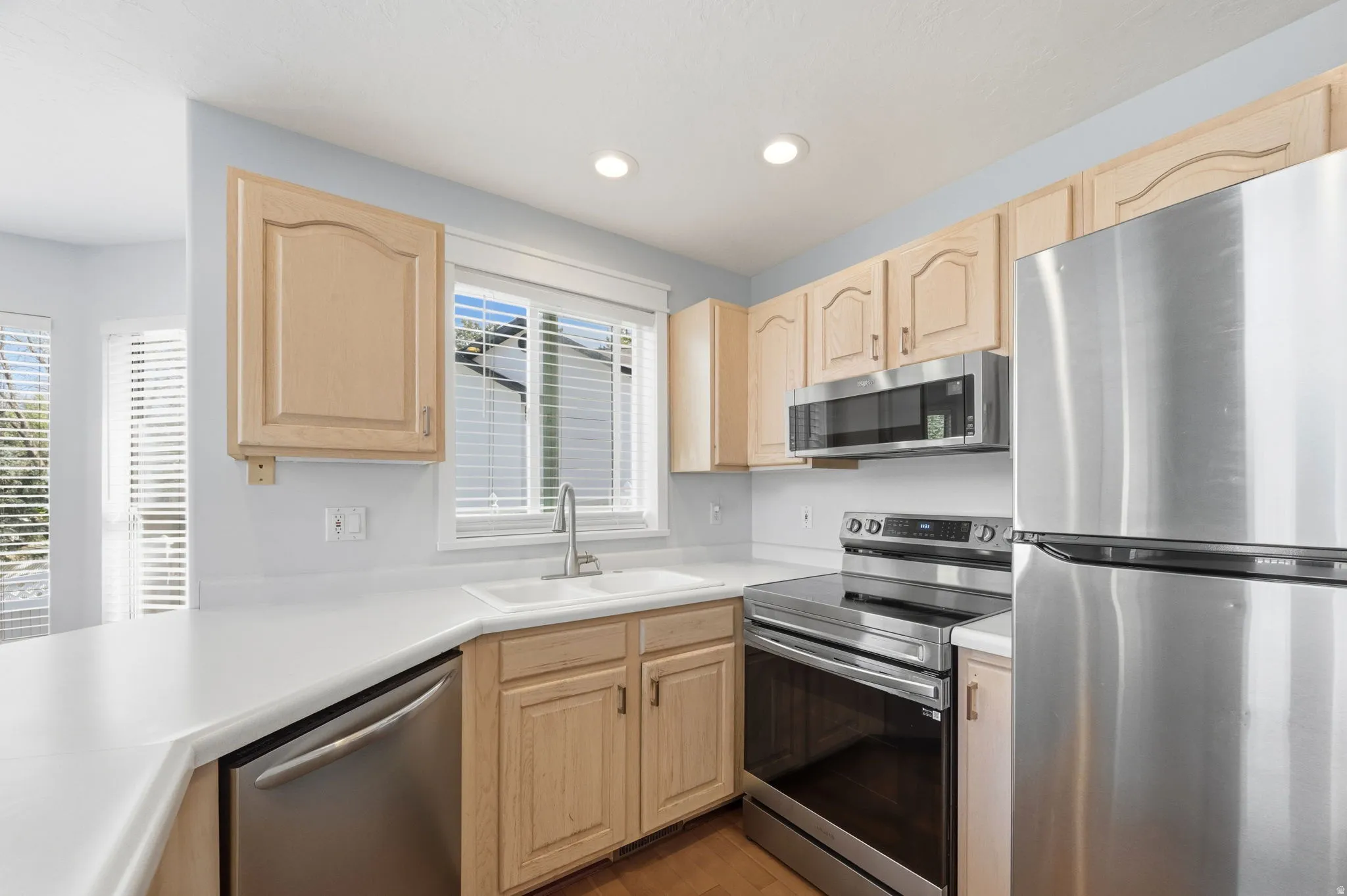 Bright kitchen featuring light wood cabinetry, white countertops, and stainless steel appliances