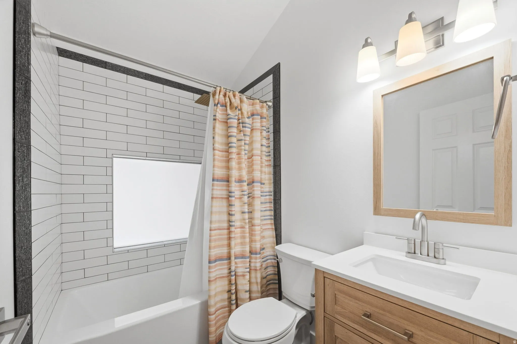 Bathroom featuring a wood-finish vanity with a white countertop and undermount sink, a framed mirror, and a three-light vanity fixture