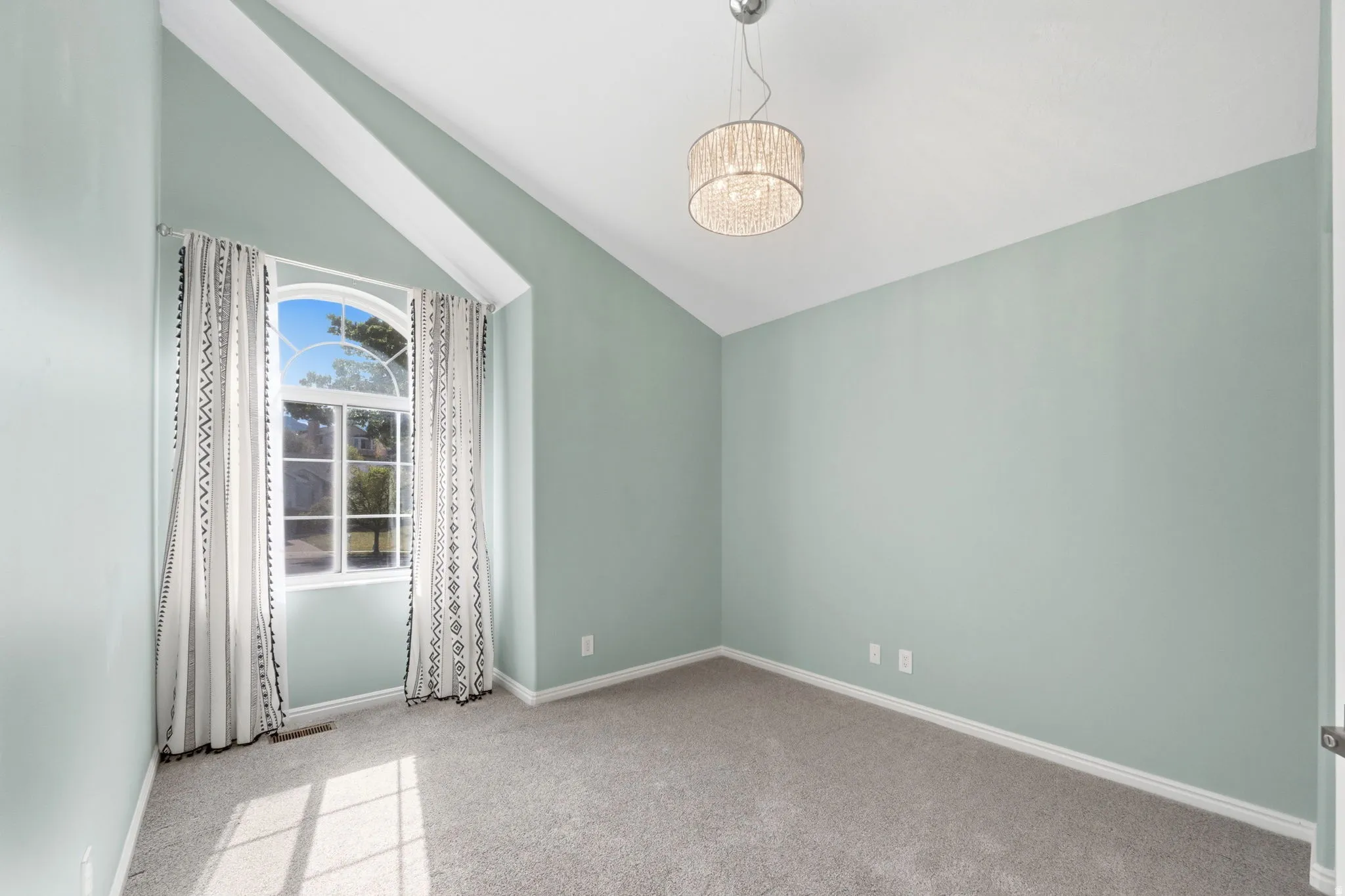 Vaulted ceiling room featuring an arched window, decorative light fixture, and neutral carpeting