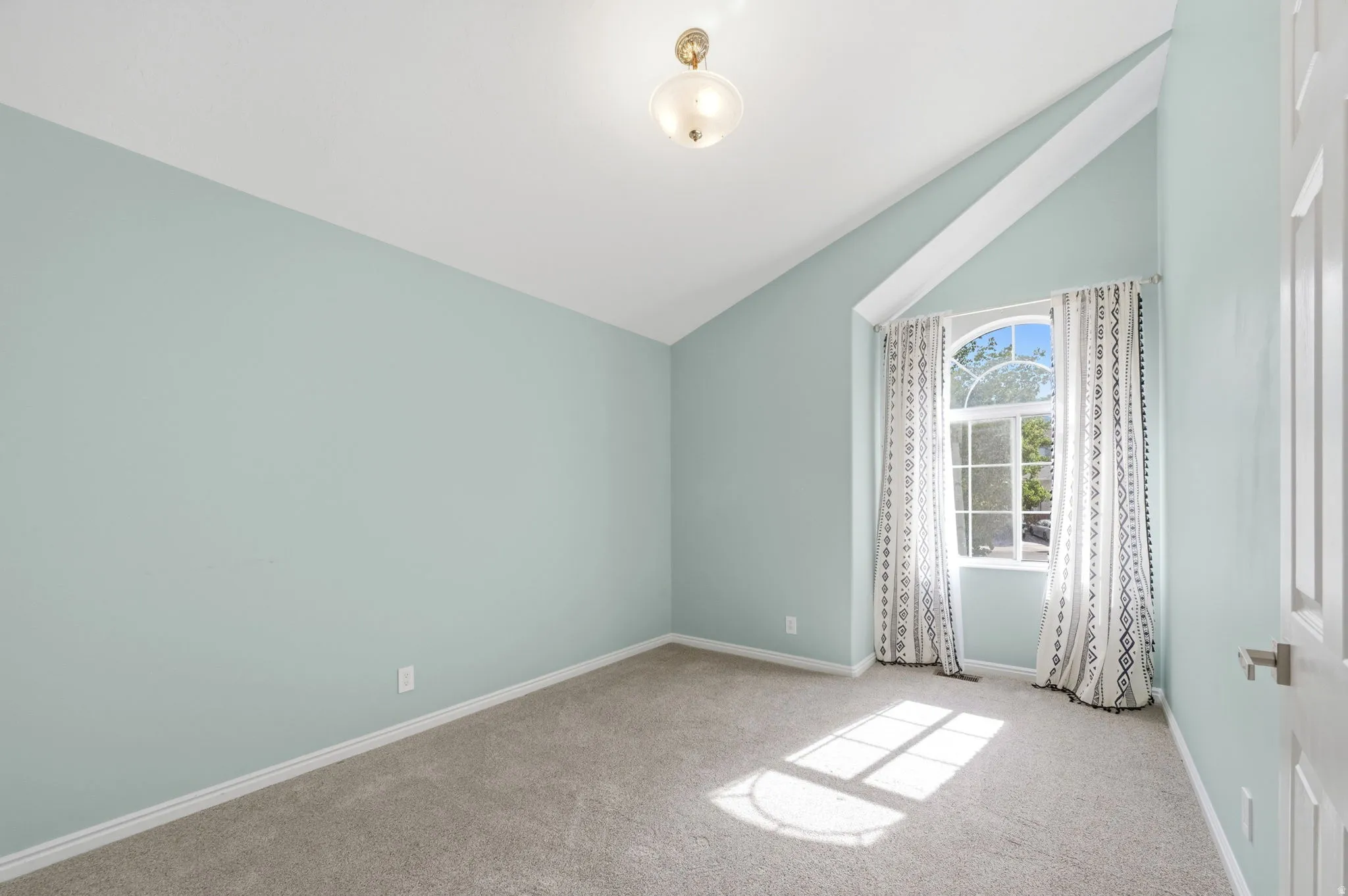 Spacious room featuring vaulted ceilings, a large arched window, wall-to-wall carpeting, light blue wall paint, and a built-in ceiling light fixture