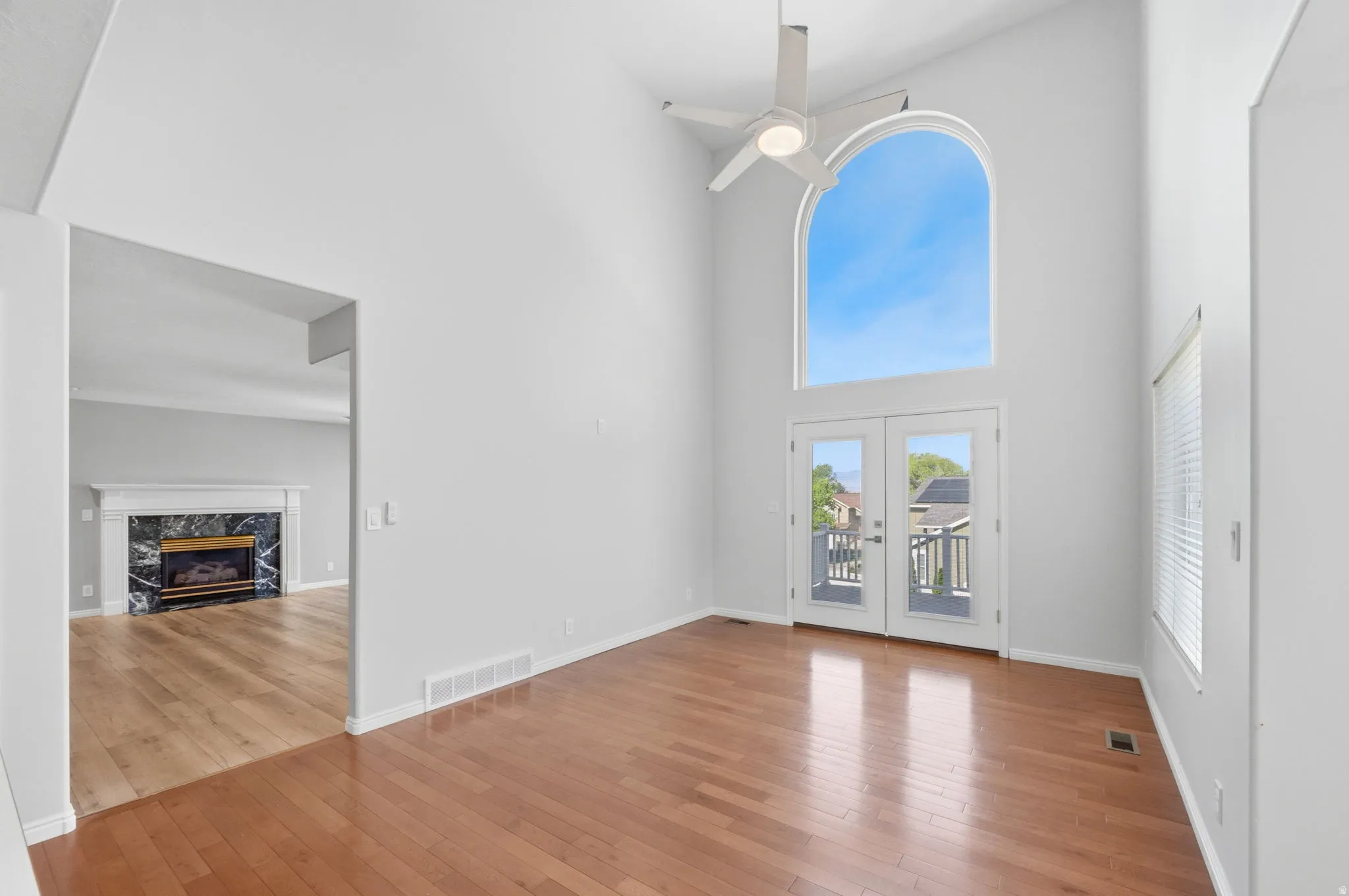 Vaulted ceiling featuring a contemporary ceiling fan, an arched picture window, and a pair of French doors opening to a deck