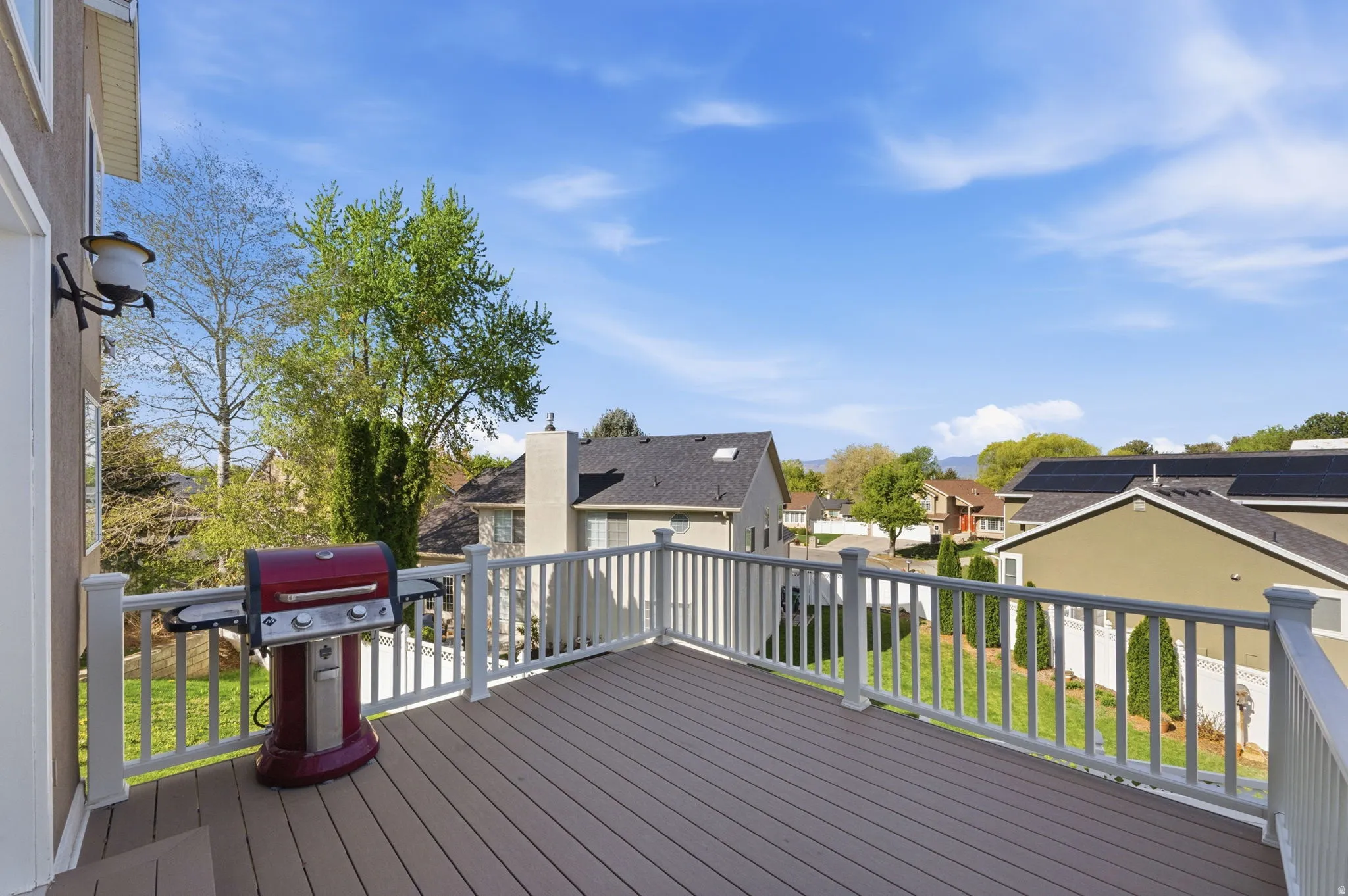 Spacious outdoor deck featuring composite decking, white railing, and a wall-mounted exterior light fixture