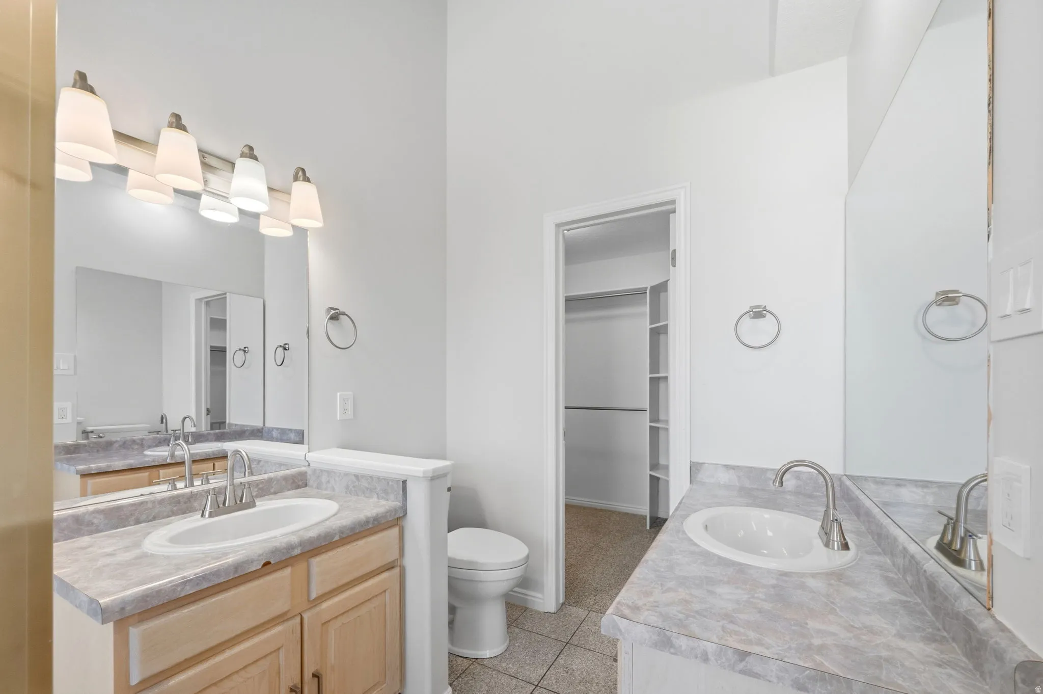 Bathroom featuring dual vanity sinks with brushed nickel fixtures, light wood-finish cabinetry, and patterned countertops