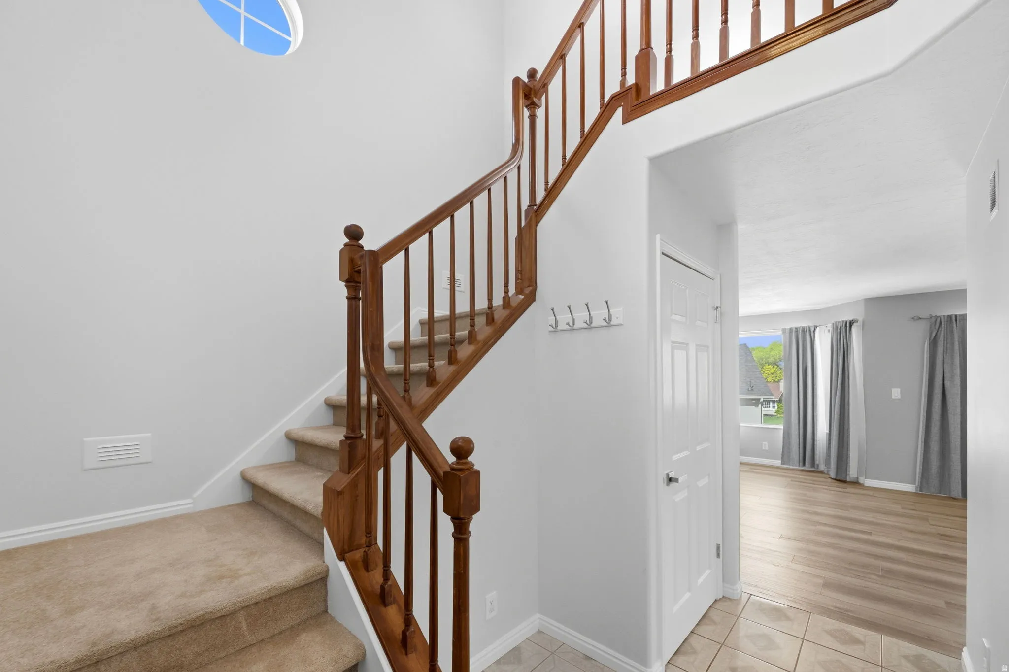 Carpeted staircase with wood-finish railings, showcasing an overhead oval window