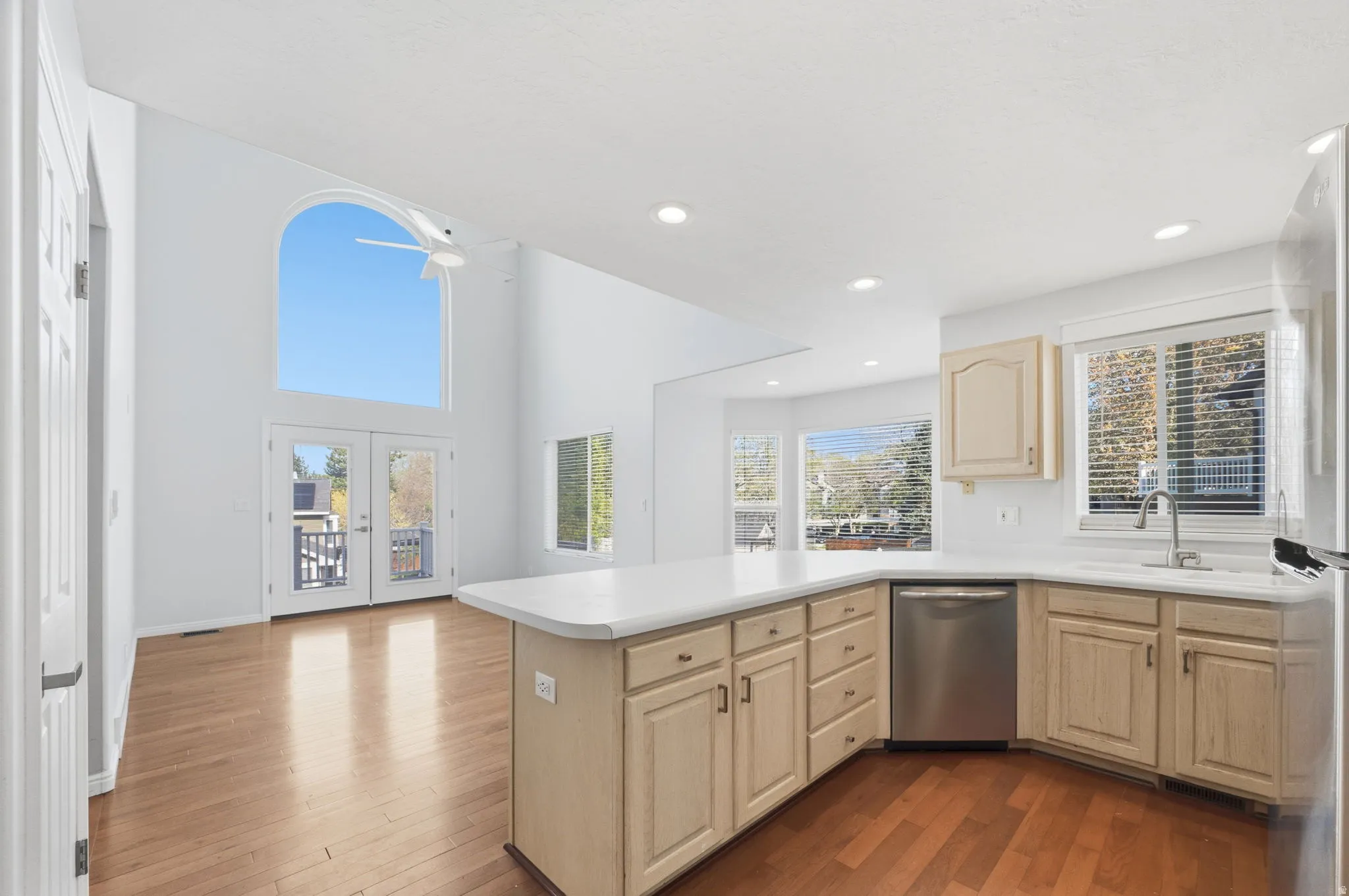 Kitchen and living area featuring high ceilings, wood-finish flooring, a kitchen island with a light-toned countertop, stainless steel dishwasher, and French doors with an arched transom window