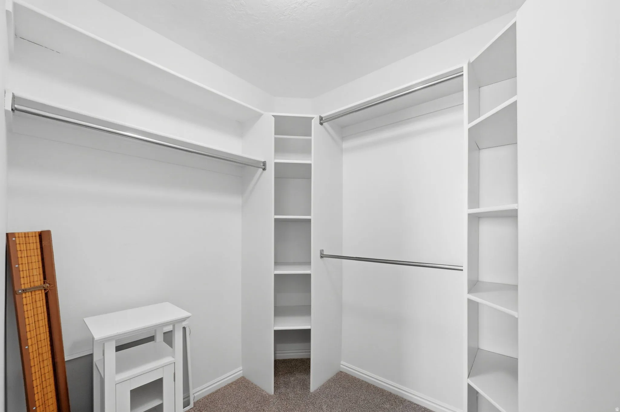 Walk-in closet featuring white built-in shelving, multiple hanging rods, and neutral carpet flooring