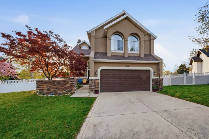 Stucco exterior with stone accents, featuring a two-car garage, arched windows, and a mature red-leaf tree