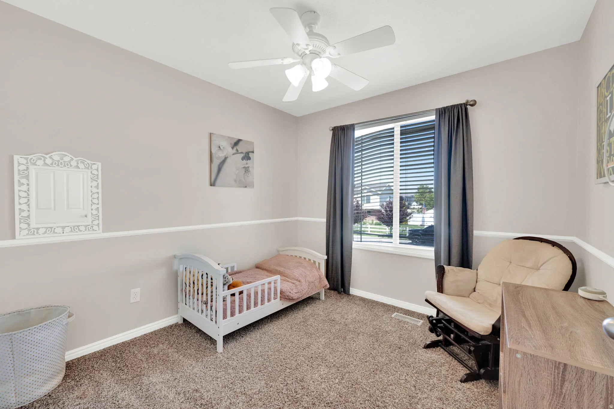 Carpeted room featuring a ceiling fan with integrated lighting, a window with blinds and drapes, and neutral two-tone wall paint with a chair rail