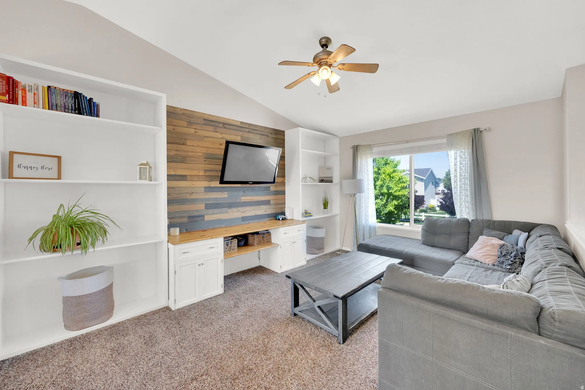 Living area featuring a vaulted ceiling with a ceiling fan, a large window, and carpet flooring