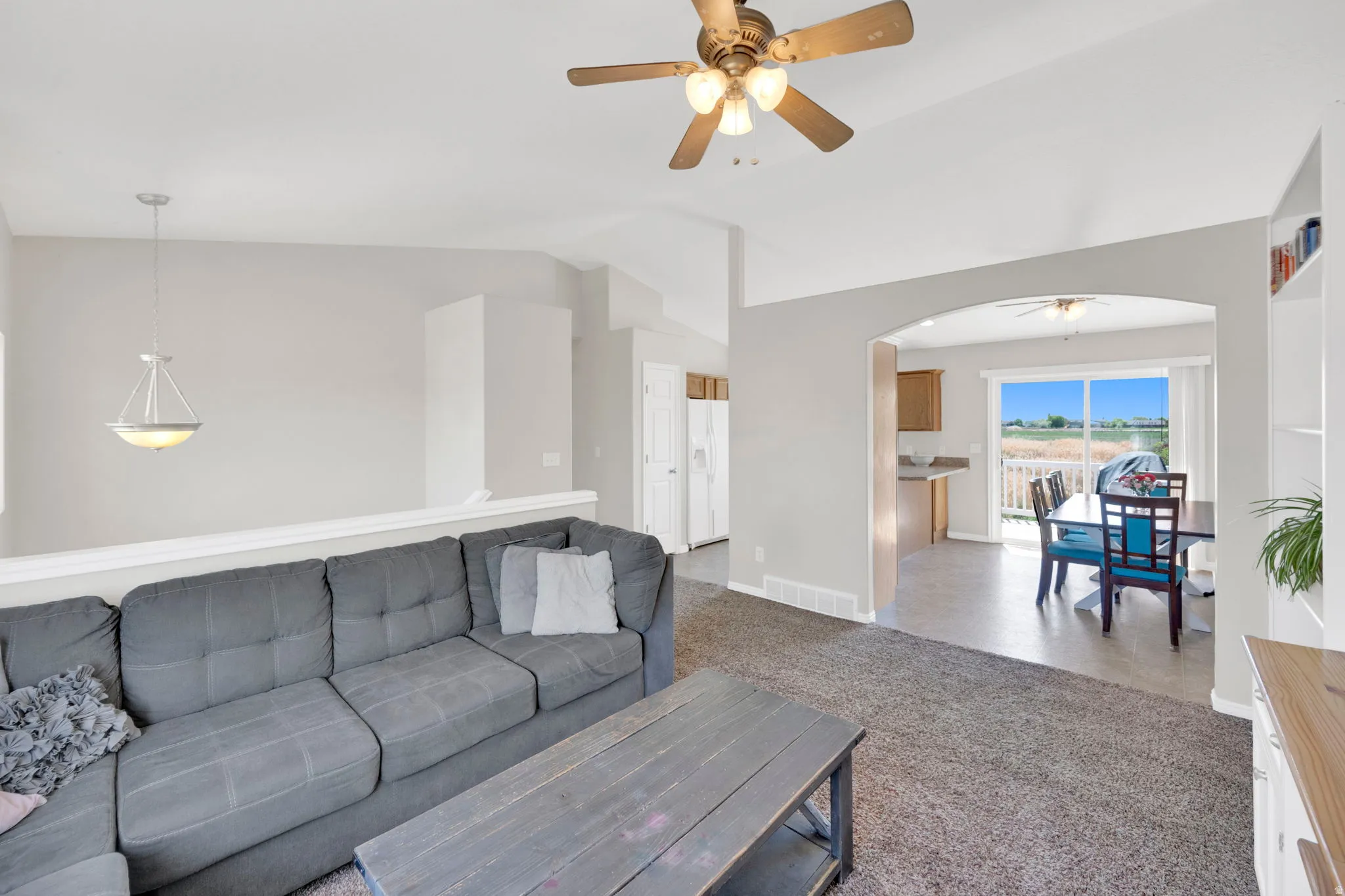 Living area featuring a textured carpet floor, vaulted ceiling, and a ceiling fan