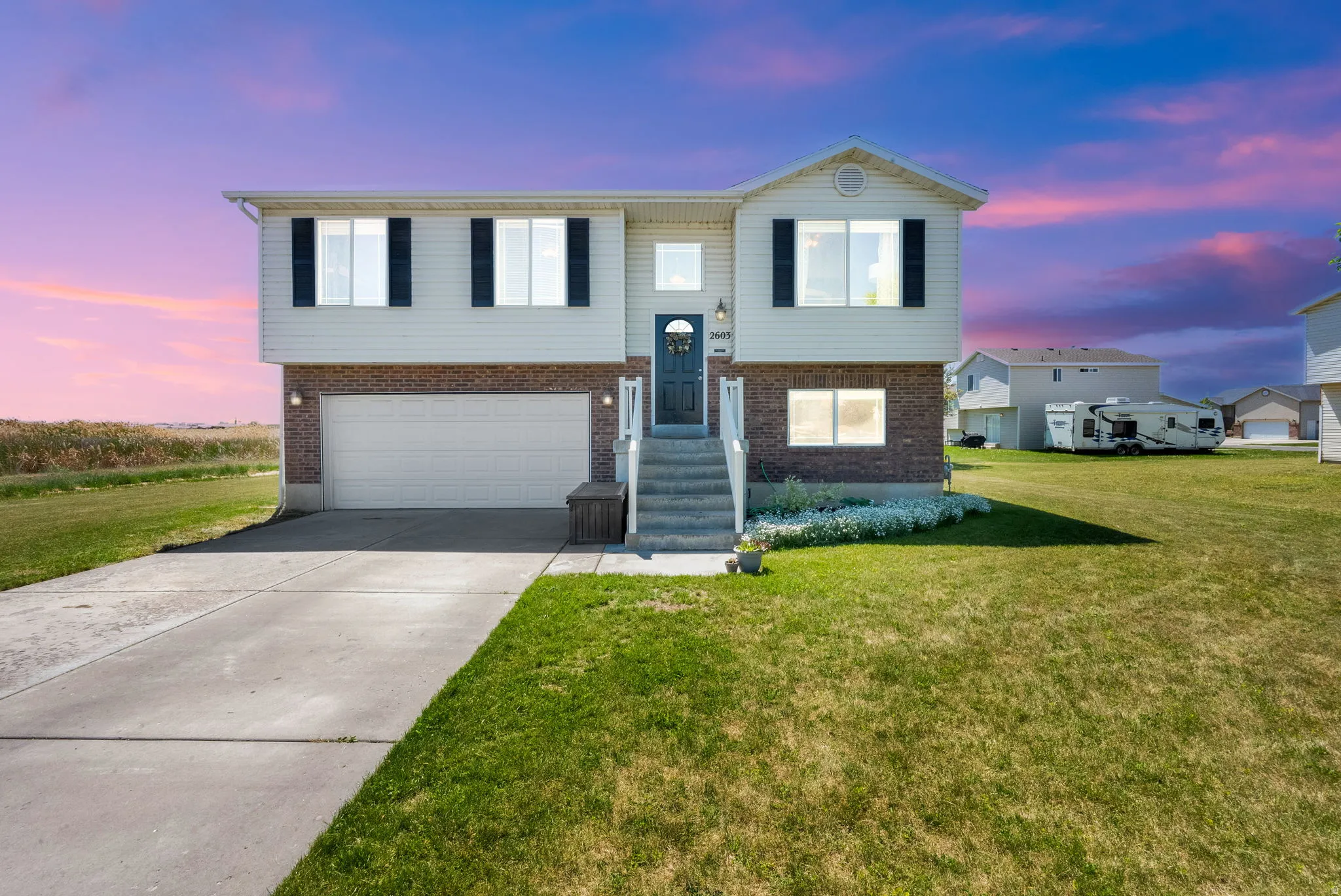 Split-level residence featuring a two-car garage, brick and siding exterior, concrete driveway, and a front porch with stairs
