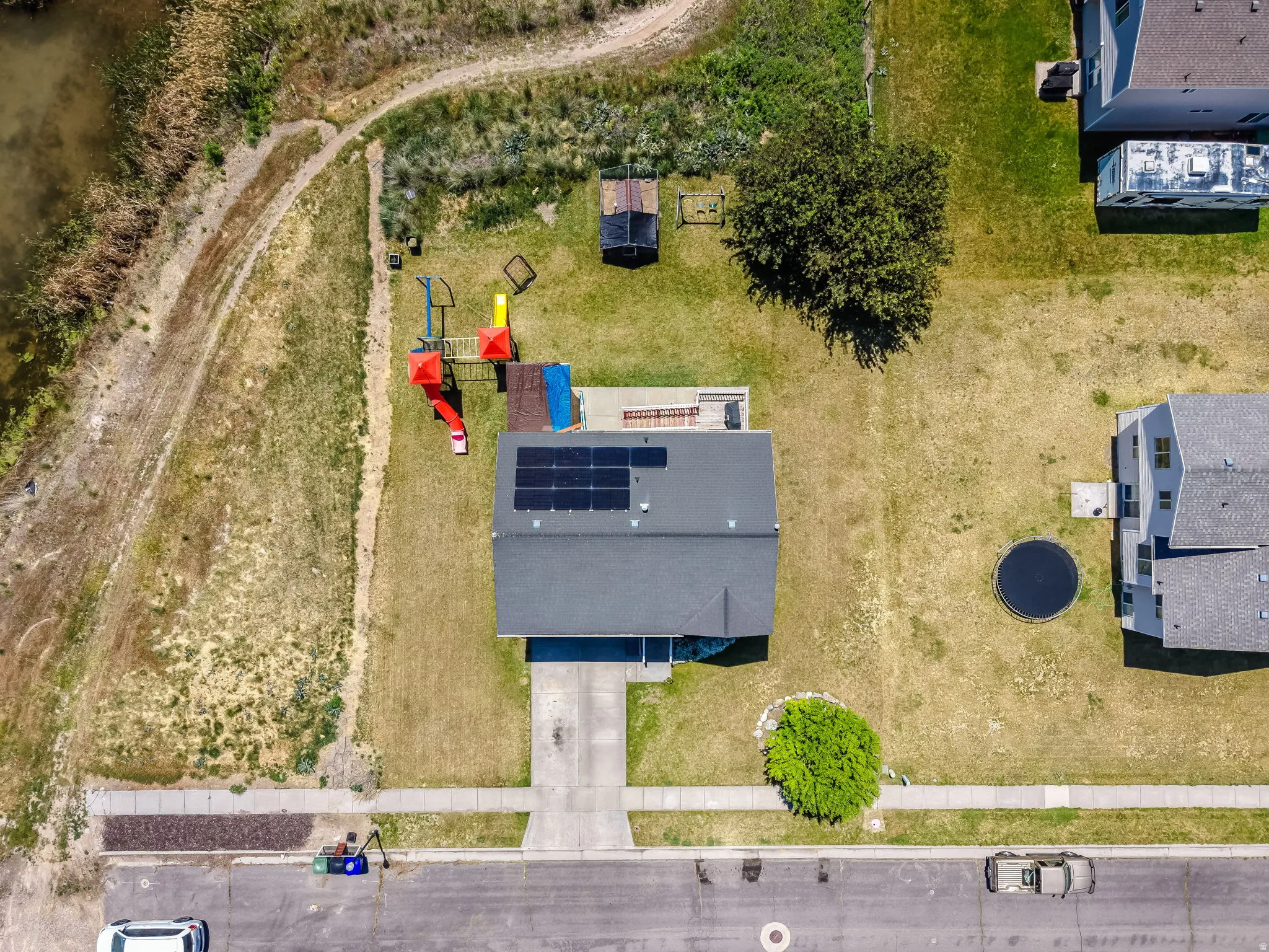 Aerial perspective showcasing a residential property with solar panels, a paved driveway, and a spacious backyard featuring a patio and green space