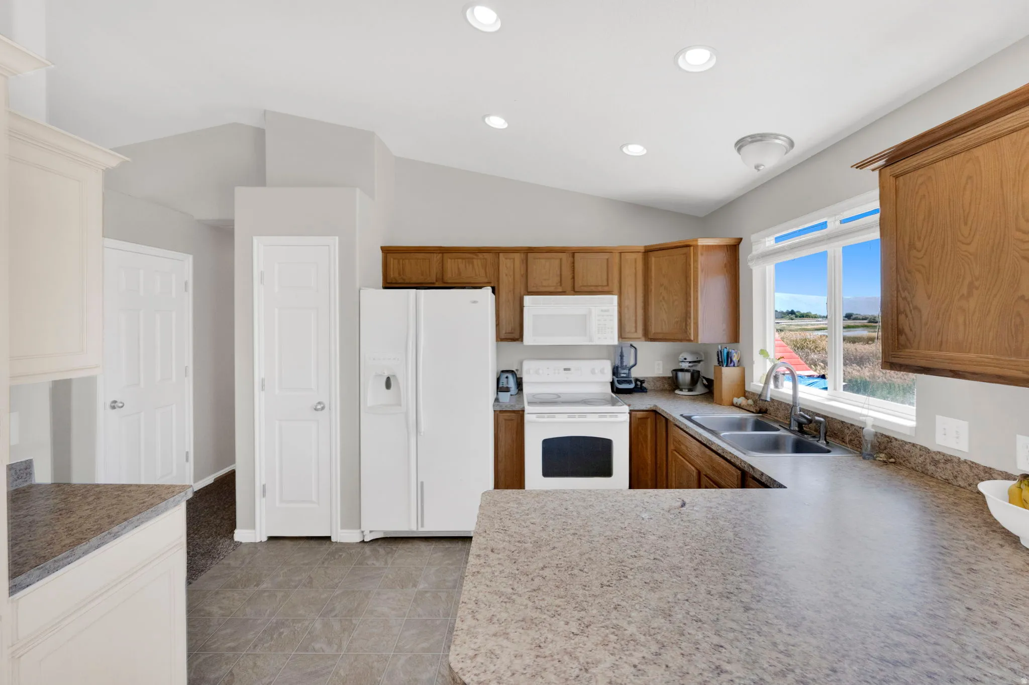 Spacious kitchen featuring warm wood cabinetry, neutral countertops, and white appliances