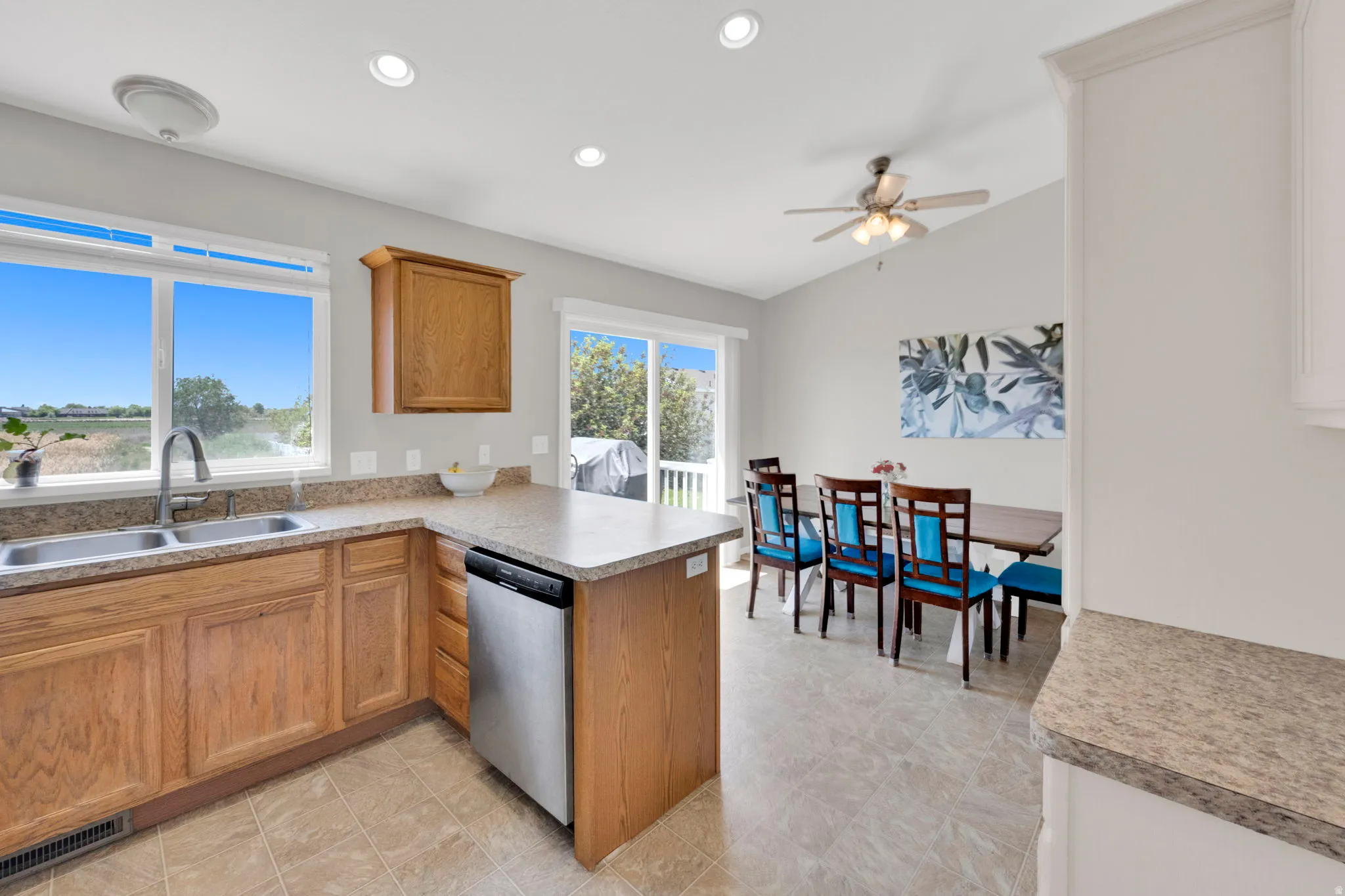 Kitchen and dining area featuring a double basin stainless steel sink, wood cabinetry, stainless steel dishwasher, and a vaulted ceiling