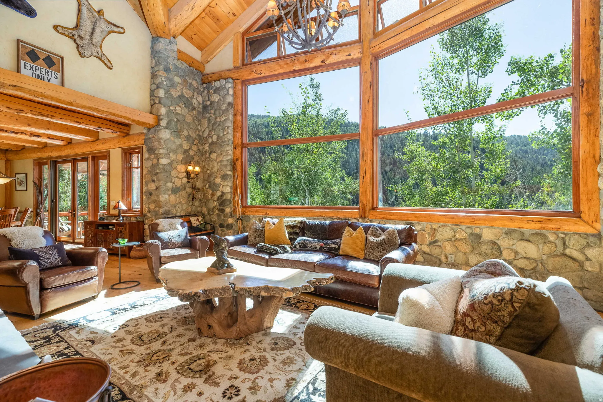 Spacious living area featuring floor-to-ceiling windows, exposed timber beams, a stone fireplace, and wood-finish flooring