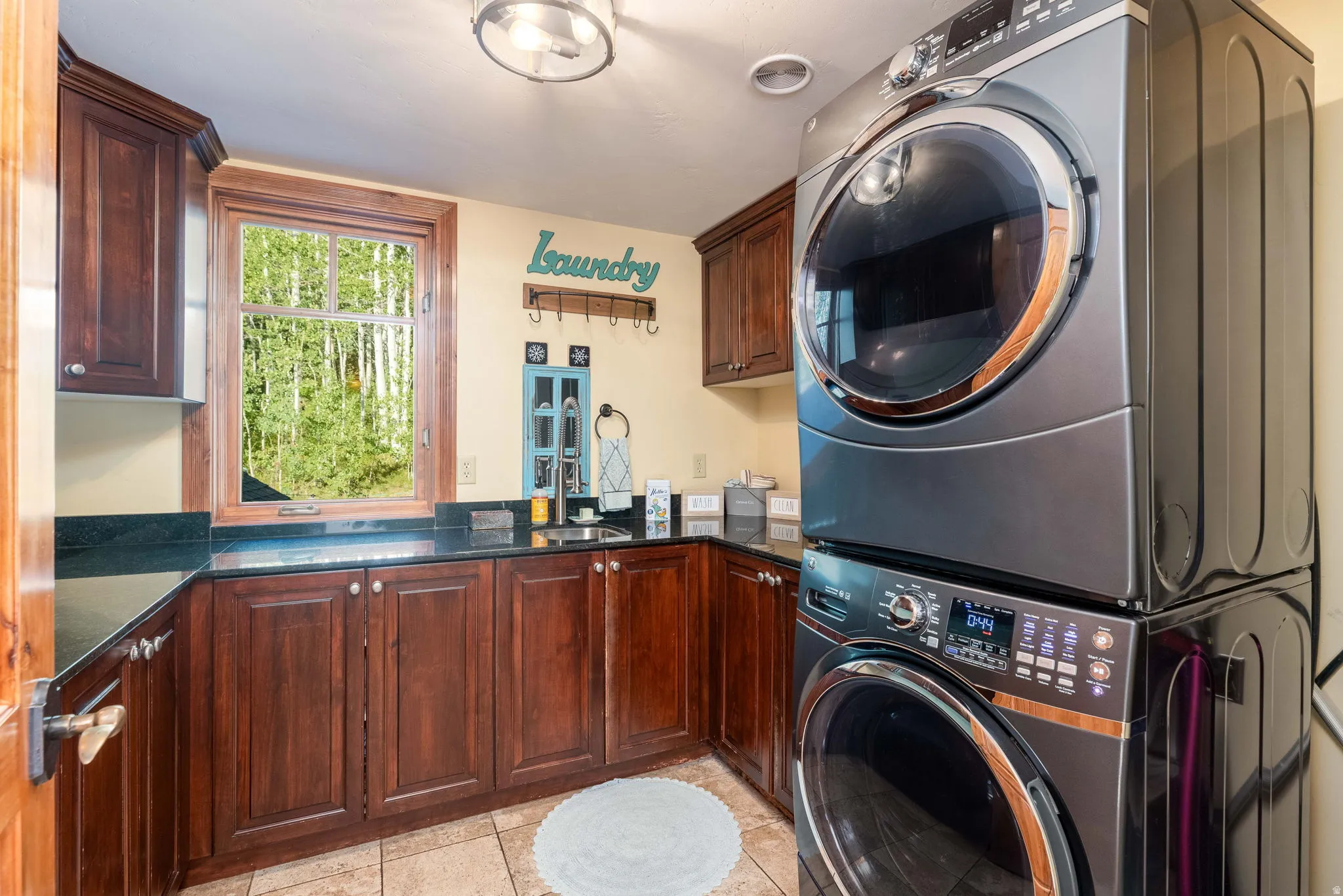 Laundry room featuring a full-size stacked washer and dryer, dark wood cabinetry, and dark countertop surfaces