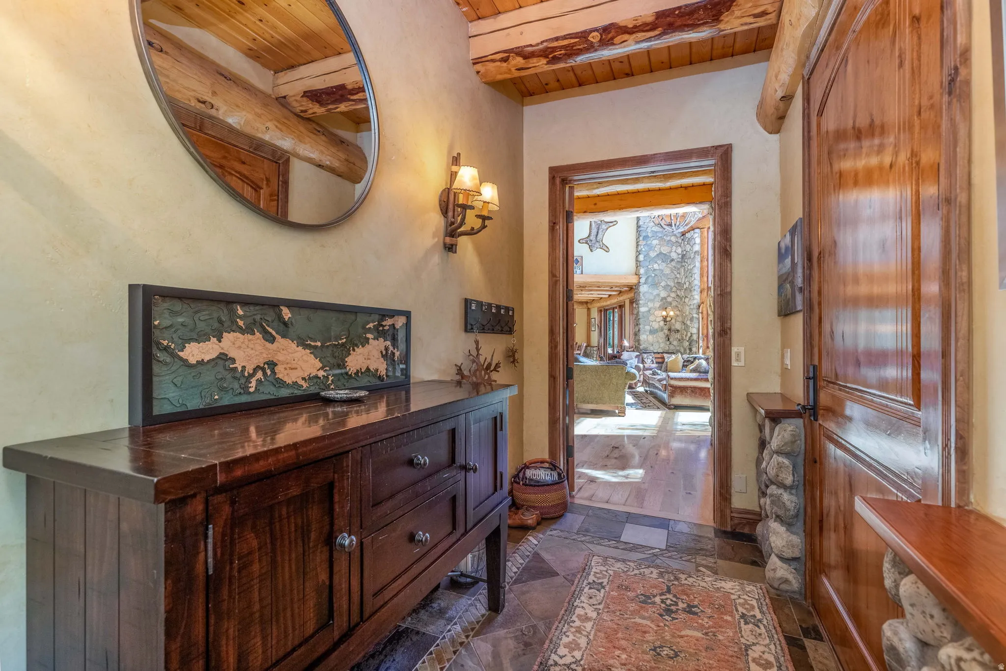 Entryway featuring wood-finish flooring with stone tile accents, a robust wood beam ceiling, and a wall-mounted sconce