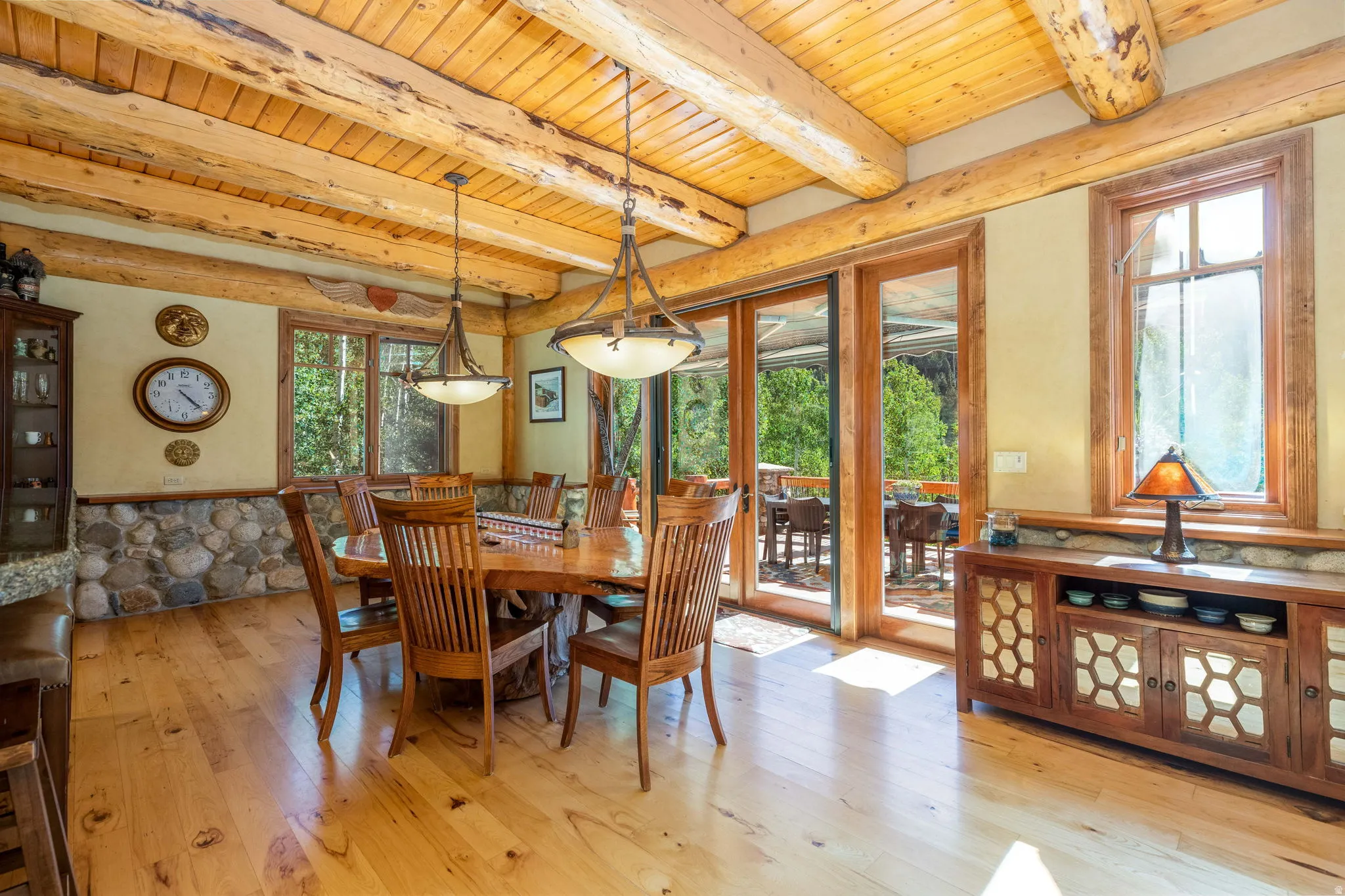 Spacious interior featuring exposed log beams, light wood-finish flooring, and a stone accent wall